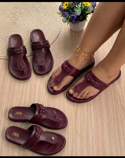 Burgundy sandals on a wooden floor with a small plant in the background